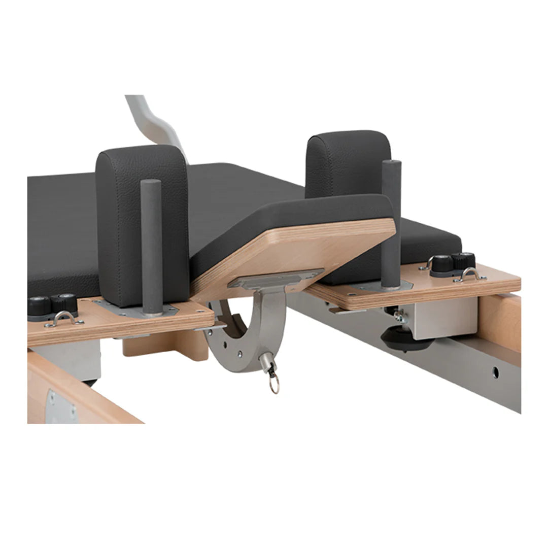 Close-up of the BASI Systems Reformer Combo's spring-loaded pulley system with wooden push-through bar and adjustable tower frame used for Pilates exercises.