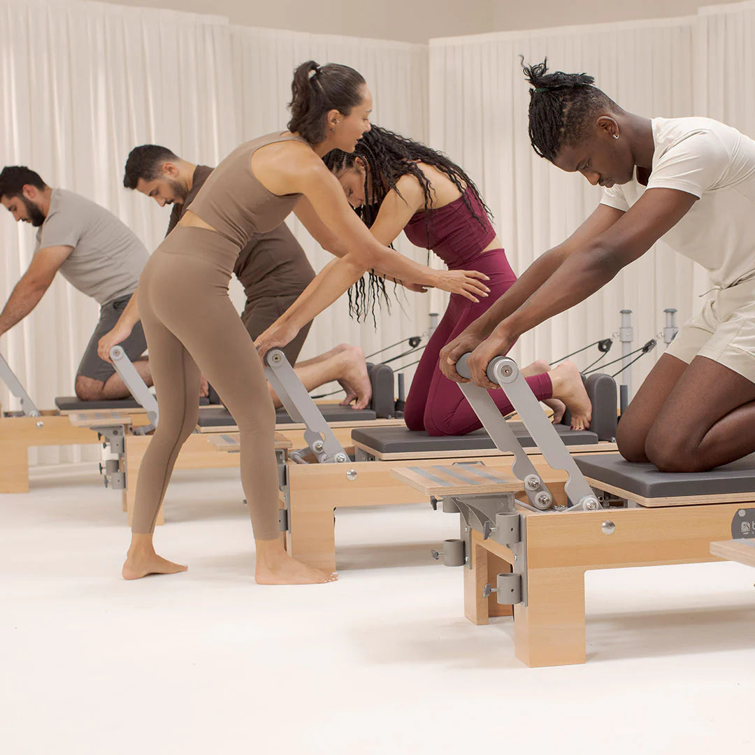 A man and woman are seated on a Pilates reformer, engaged in a workout session together.