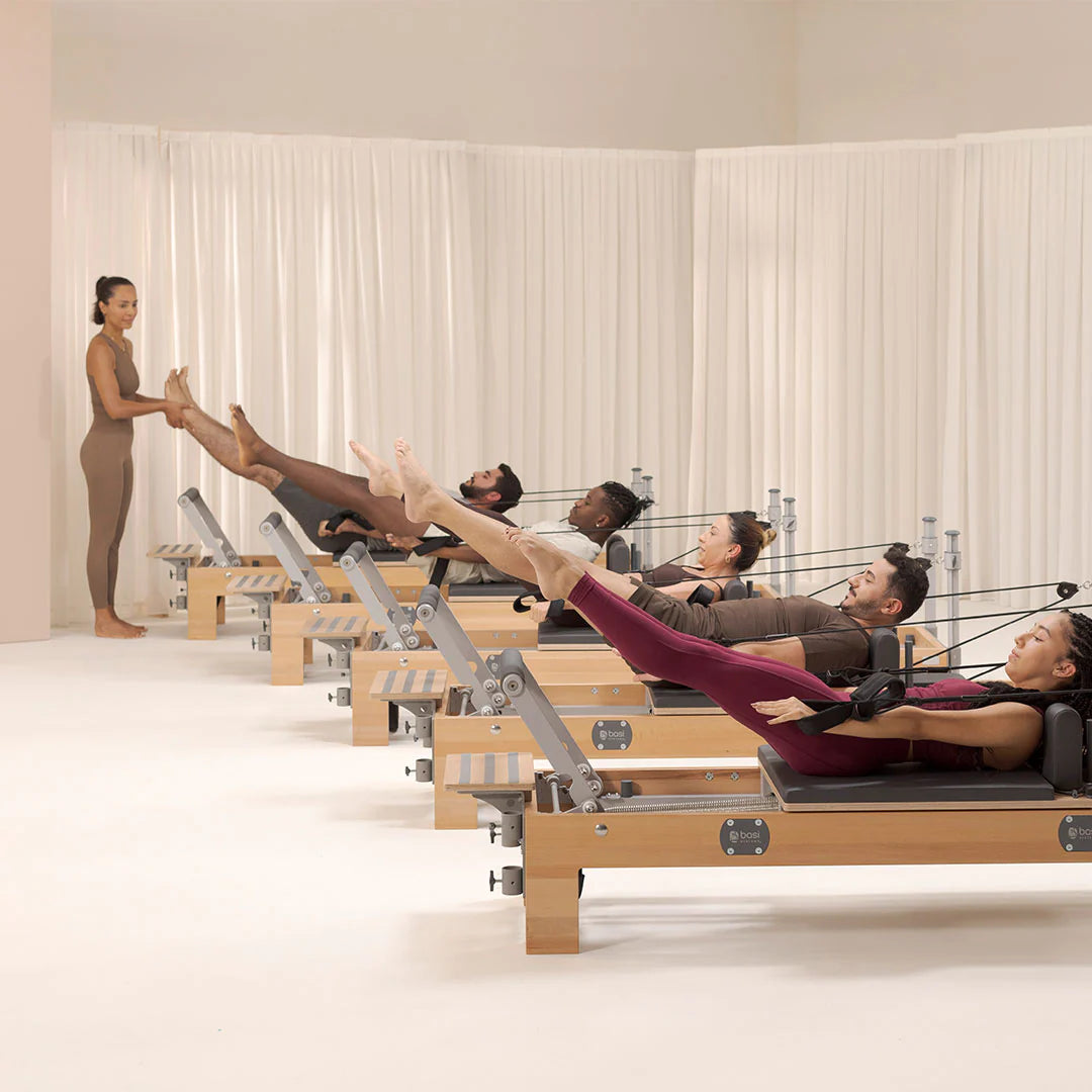 A man and woman are seated on a Pilates reformer, engaged in a workout session together.