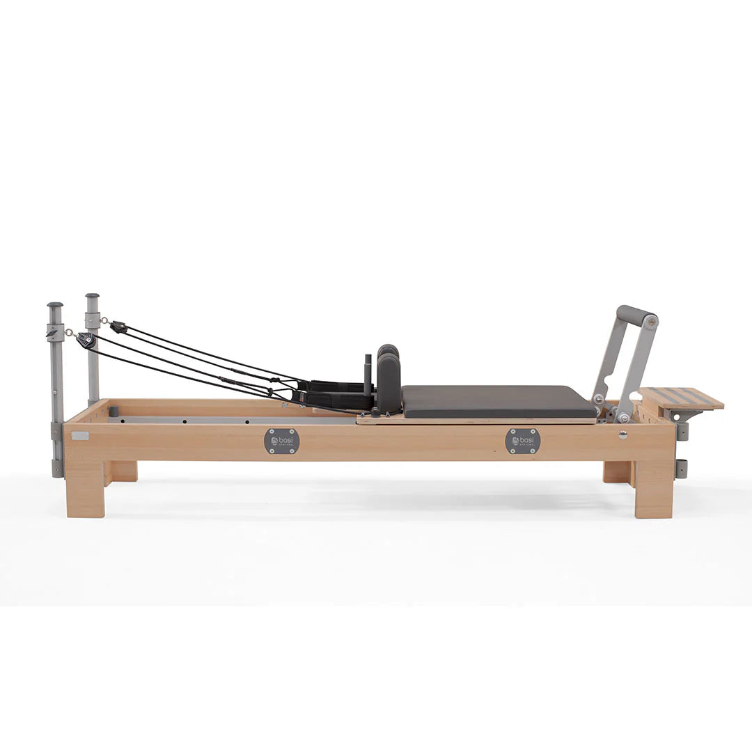 A pilates reformer featuring a padded seat and adjustable footrest for various exercises.