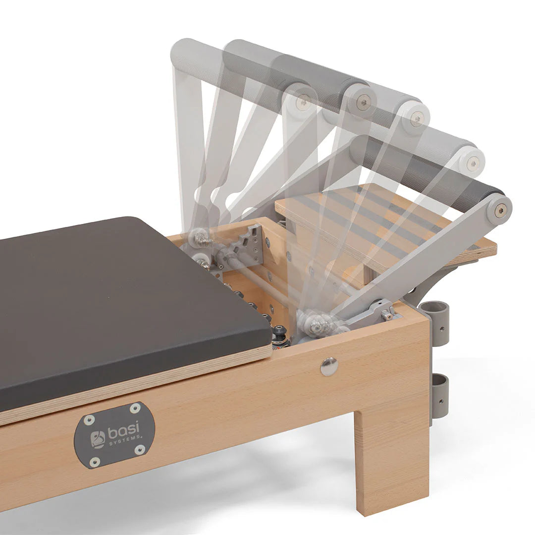 A pilates reformer featuring a padded seat and adjustable footrest for various exercises.