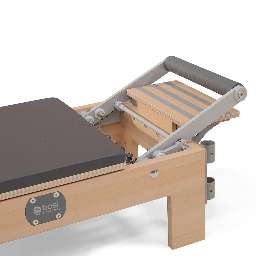 A pilates reformer featuring a padded seat and adjustable footrest for various exercises.