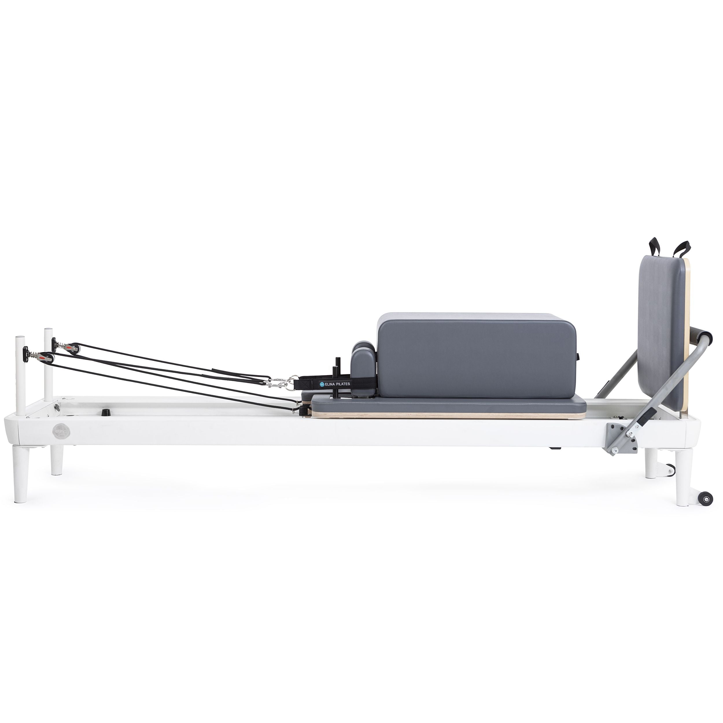 A pilates reformer featuring a padded seat and adjustable footrest for various exercises.