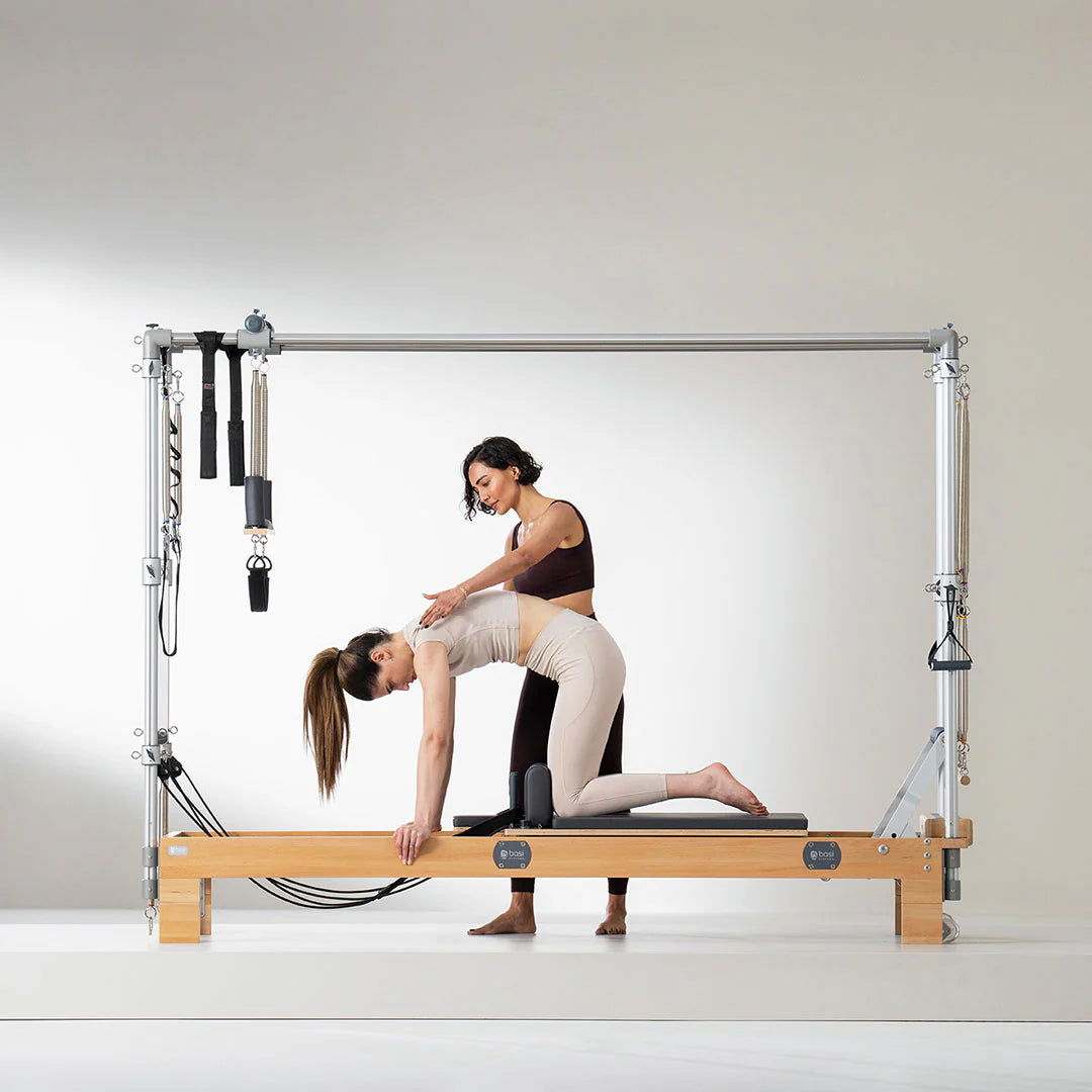 Instructor guiding a woman on a Pilates reformer combo machine during a fitness session.