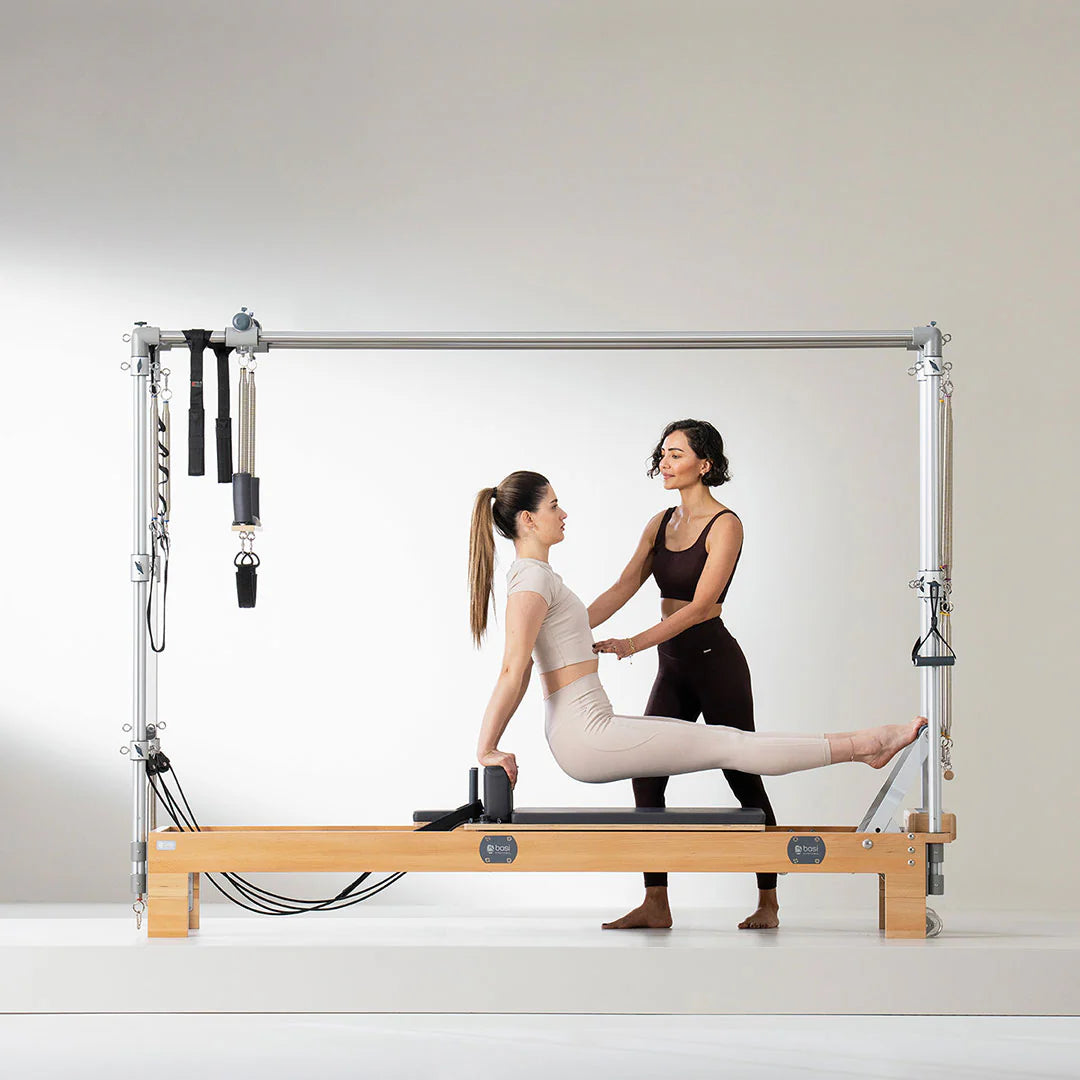 Instructor guiding a woman on a Pilates reformer combo machine during a fitness session.