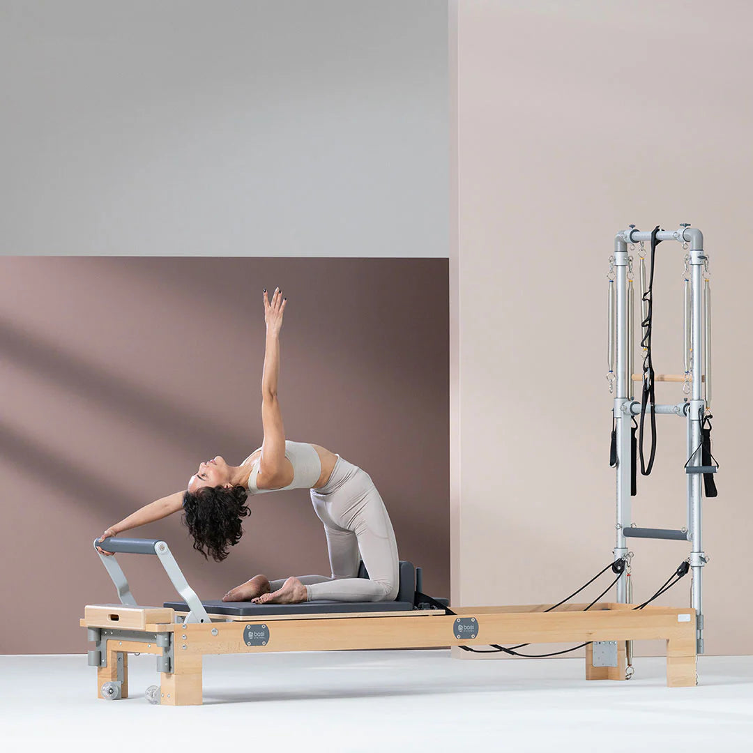 A woman is practicing Pilates on the Wellness Reformer with Tower, showcasing her technique and concentration in the exercise.