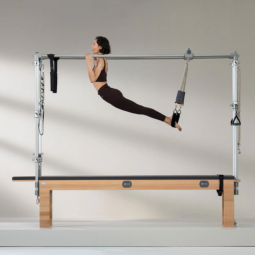 Woman performing advanced Pilates exercise on BASI Cadillac Trapeze Table using push-through bar and fuzzy loops for suspension training