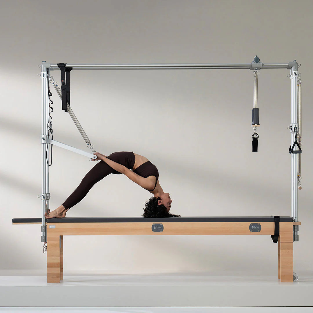 Woman performing advanced Pilates exercise on BASI Cadillac Trapeze Table using push-through bar and fuzzy loops for suspension training