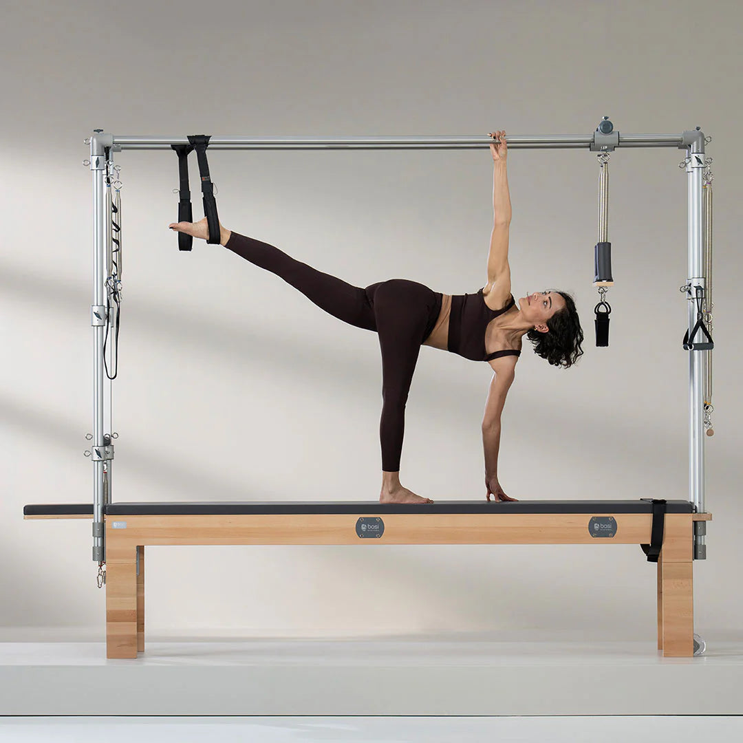 Woman performing advanced Pilates exercise on BASI Cadillac Trapeze Table using push-through bar and fuzzy loops for suspension training